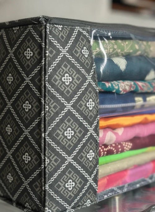A close-up of a black fabric storage box with a white geometric pattern and a clear zippered top, showing folded colorful textiles inside.